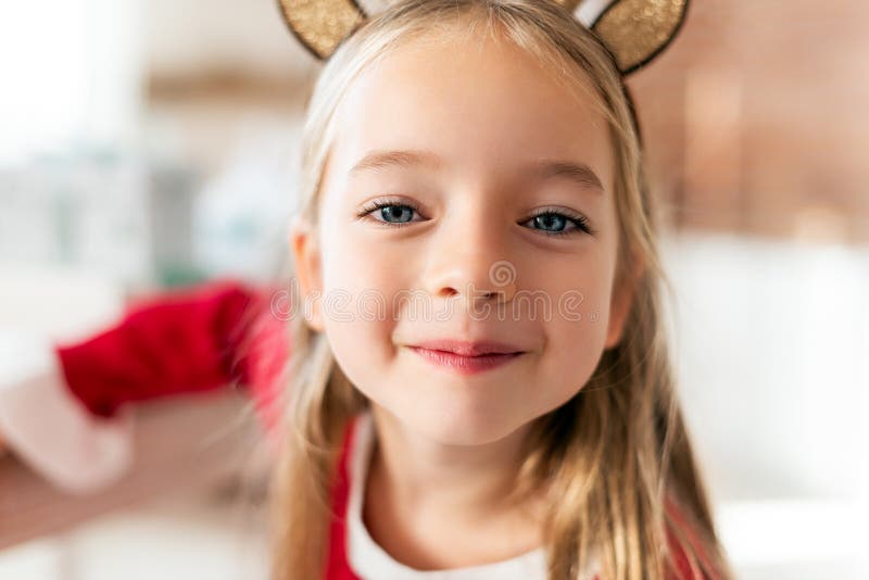 För dräktren för gullig ung flicka bärande horn på kronhjort och att le och se kameran Lycklig unge på jul royaltyfria bilder