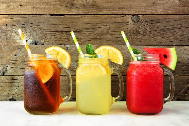 För fruktsaftsommar för med is te, lemonad- och vattenmelondrinkar i exponeringsglas för murarekrus mot mörkt trä