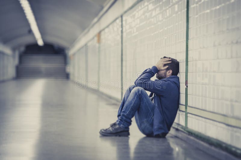 Young man drug addict homeless and abandoned lost in depression sitting on ground street subway tunnel suffering mental disorder, emotional pain, sadness and looking sick and desperate leaning on wall alone. Young man drug addict homeless and abandoned lost in depression sitting on ground street subway tunnel suffering mental disorder, emotional pain, sadness and looking sick and desperate leaning on wall alone