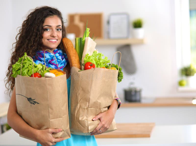Young woman holding grocery shopping bag with vegetables . Standing in the kitchen. Young woman holding grocery shopping bag with vegetables . Standing in the kitchen.
