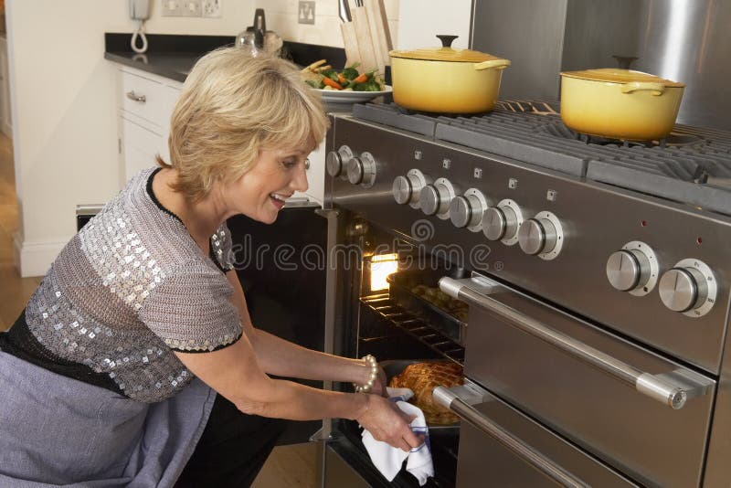 Woman In Kitchen Taking Food Out Of The Oven. Woman In Kitchen Taking Food Out Of The Oven