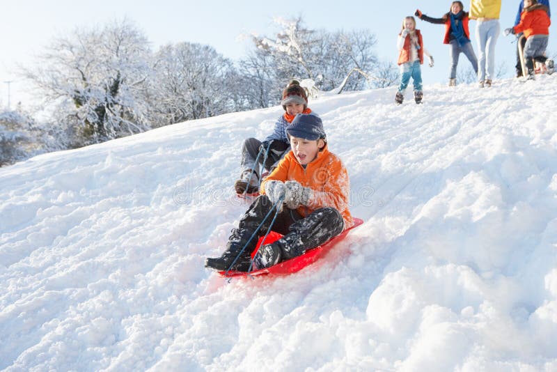 Young Boy Sledging Down Hill With Family Watching Having Fun. Young Boy Sledging Down Hill With Family Watching Having Fun