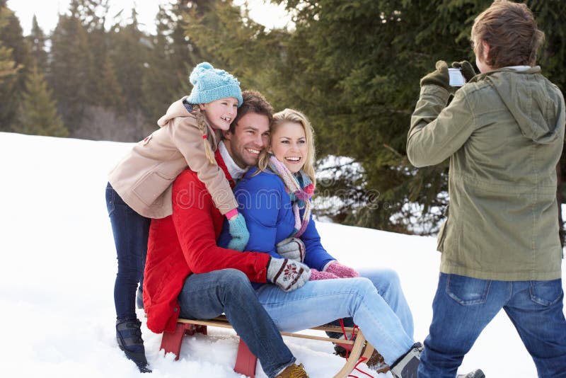 Young Family Sitting On A Sled In The Snow smiling having picture taken. Young Family Sitting On A Sled In The Snow smiling having picture taken