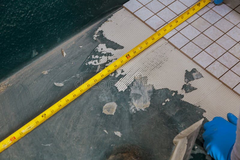 Fördelande våt mortel, innan att applicera tegelplattor på badrumgolvarbetaren som använder att mäta och att markera arkivbild Fördelande våt mortel, innan att applicera tegelplattor på badrumgolvarbetaren som använder att mäta och att markera arkivbild