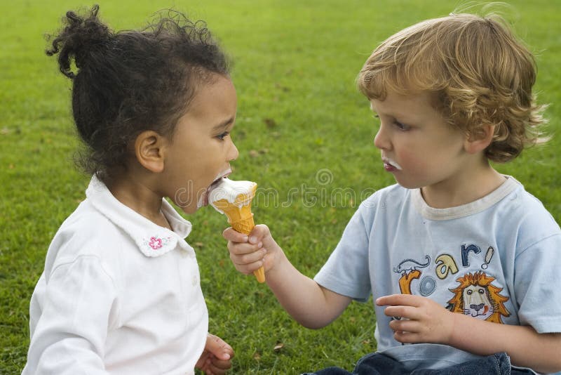 Two children, one a blond boy, one a mixed race girl sharing an ice cream. Two children, one a blond boy, one a mixed race girl sharing an ice cream