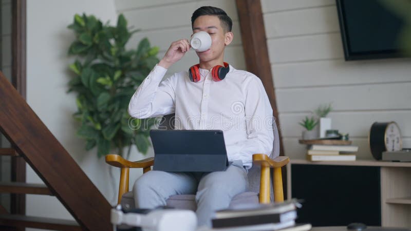 Förhandsvisning av glad, stilig, ung, man som dricker morgonkaffe i vardagsrum surfar på internet på internet stock video