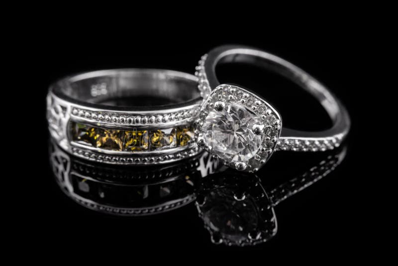 Silver or white gold engagement rings with yellow gems and diamonds on black glass background. Silver or white gold engagement rings with yellow gems and diamonds on black glass background