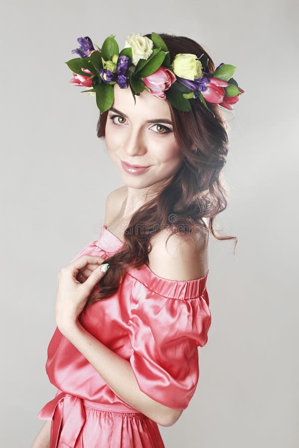 Försiktigt romantiskt utseende av flickan med en krans av rosor på hennes huvud och en rosa klänning Glad glad vårkvinna Sommarda arkivfoto Försiktigt romantiskt utseende av flickan med en krans av rosor på hennes huvud och en rosa klänning Glad glad vårkvinna Sommarda arkivfoto