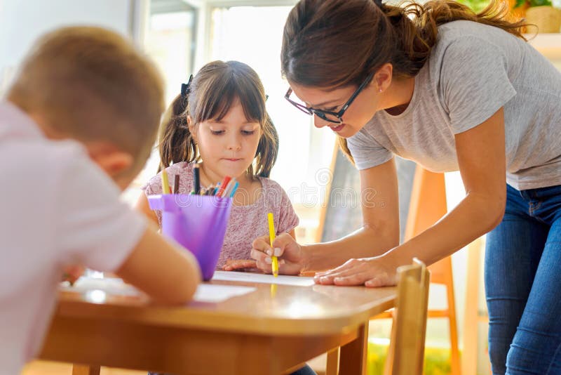 Förskole- lärare som ser det smarta barnet som lär att skriva och dra arkivbild