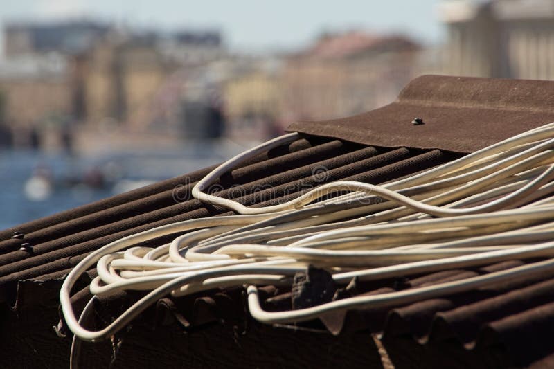 Fragment of a roof in the city center with white wires lying on it, forming an interesting pattern against the background of the roof covering and semi-blurred buildings of classical city architecture in the background, cityscape, vintage look, electrical wires, sunlight, deto. Fragment of a roof in the city center with white wires lying on it, forming an interesting pattern against the background of the roof covering and semi-blurred buildings of classical city architecture in the background, cityscape, vintage look, electrical wires, sunlight, deto.