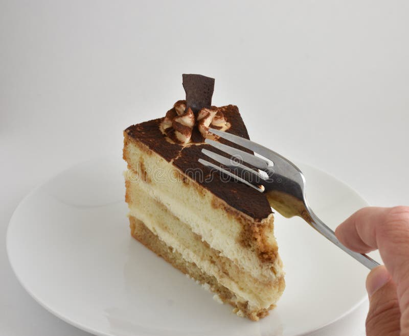 First bite showing a fork cutting a Tiramisu layered cake on white plate with chocolate powder, swirled icing, white background. First bite showing a fork cutting a Tiramisu layered cake on white plate with chocolate powder, swirled icing, white background.