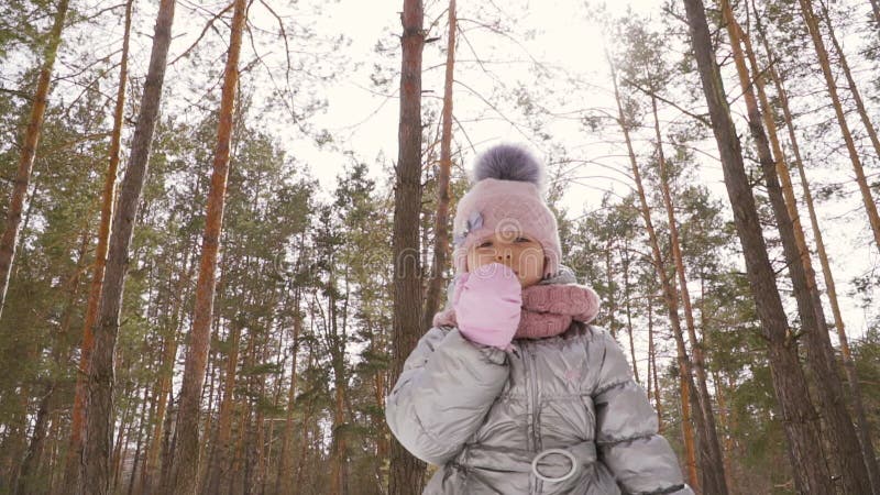 Förtjusande liten flickavåghand till kameran och vinterskogbakgrund