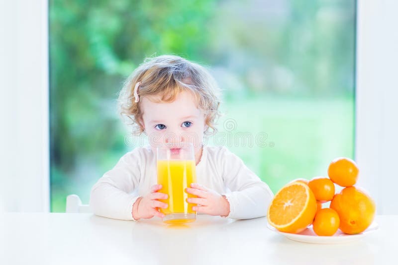 Förtjusande litet barnflicka som dricker orange fruktsaft royaltyfria foton