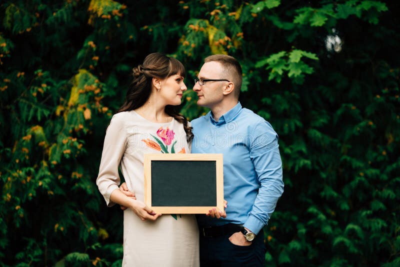 Förvänta gravida lyckliga stilfulla par som rymmer ett tomt kol, stiga ombord royaltyfria foton Förvänta gravida lyckliga stilfulla par som rymmer ett tomt kol, stiga ombord royaltyfria foton