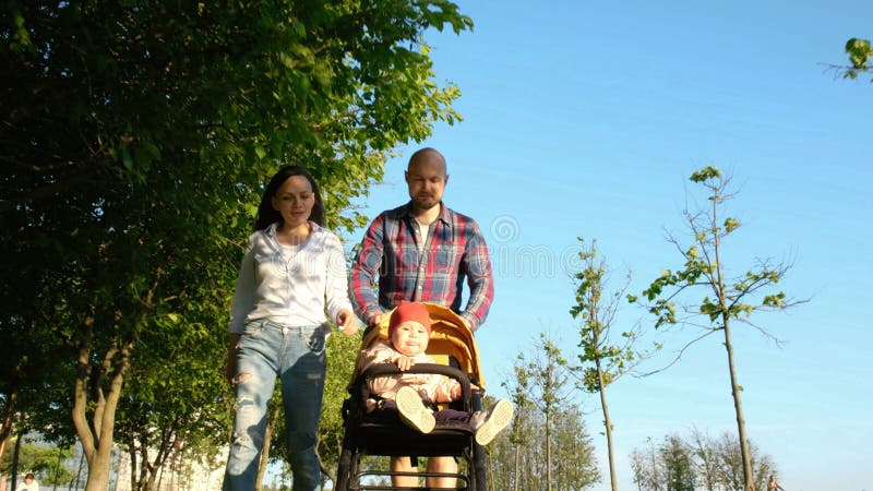 Föräldrar som går med ett barn i parkera Lycklig familj: Mamman och farsan rullade barnet i pram i natur på solnedgången royaltyfri bild Föräldrar som går med ett barn i parkera Lycklig familj: Mamman och farsan rullade barnet i pram i natur på solnedgången royaltyfri bild