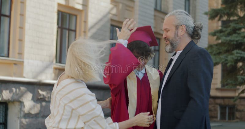 Föräldrar som kramar sonstudent i graderingsgåva och pantskola som gratulerar till campus