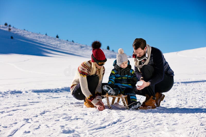 Föräldraskap, mode, säsong och folkbegrepp - lycklig familj med barnet på släden som utomhus går i vinter arkivbild Föräldraskap, mode, säsong och folkbegrepp - lycklig familj med barnet på släden som utomhus går i vinter arkivbild