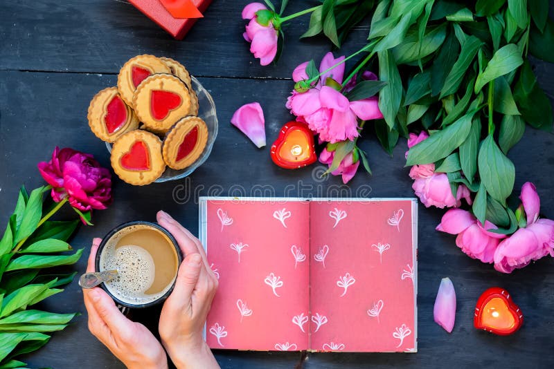 Förälskelse- och omsorgbegrepp Romantisk stil - kvinnliga händer som rymmer kaffe, rånar och öppnade anteckningsboken som omges m arkivbilder Förälskelse- och omsorgbegrepp Romantisk stil - kvinnliga händer som rymmer kaffe, rånar och öppnade anteckningsboken som omges m arkivbilder