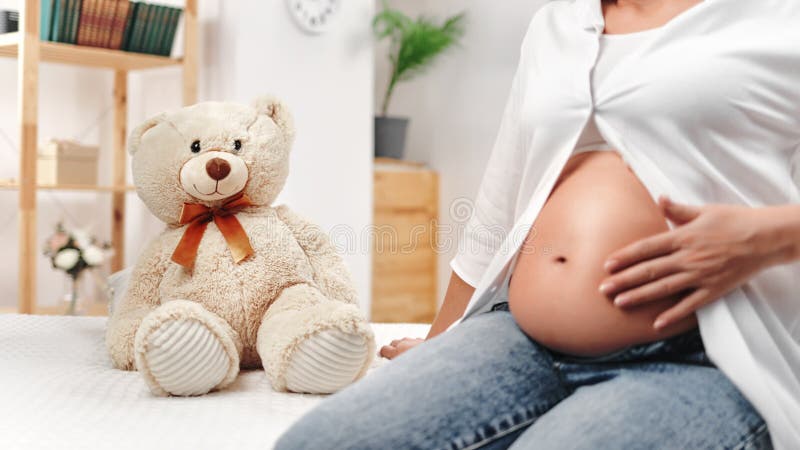 Fürsorgende zukünftige Mutter streichelt Tummy warten Baby mit Liebe und Zärtlichkeit in gemütlichen weißen Raum in der Nähe