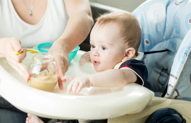 Fütterungsbaby der Mutter mit Fruchtmus auf Küche lizenzfreie stockbilder Fütterungsbaby der Mutter mit Fruchtmus auf Küche lizenzfreie stockbilder