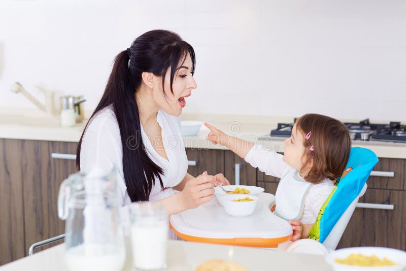Fütterungskind des Mamalöffels in der Küche familie lizenzfreie stockbilder Fütterungskind des Mamalöffels in der Küche familie lizenzfreie stockbilder