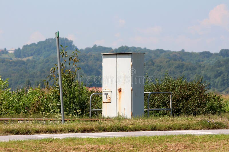 Gabinetto grigio del metallo della ferrovia all'aperto protettivo con il forte recinto del metallo accanto ai binari ferroviari fotografie stock Gabinetto grigio del metallo della ferrovia all'aperto protettivo con il forte recinto del metallo accanto ai binari ferroviari fotografie stock