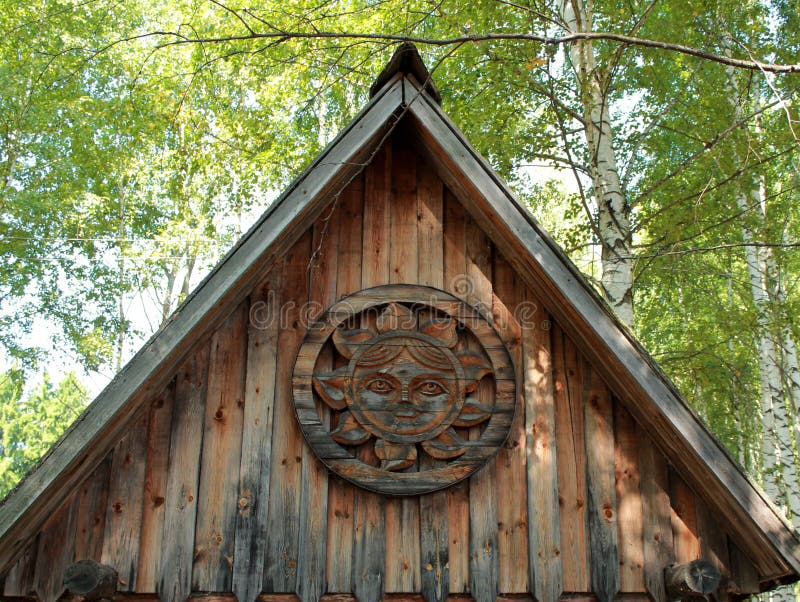 Gable old wooden house on the background of birches and blue sky