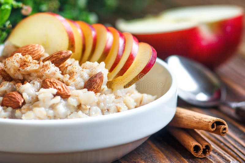 Gachas de avena orgánicas de la harina de avena en el cuenco de cerámica blanco con el desayuno sano de la manzana, de la almendr fotografía de archivo libre de regalías Gachas de avena orgánicas de la harina de avena en el cuenco de cerámica blanco con el desayuno sano de la manzana, de la almendr fotografía de archivo libre de regalías