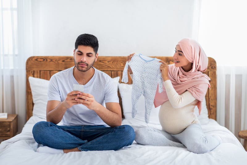 Gadgetberoendekoncept. vårdslös muslimsk man som använder smartphone och ignorerar hans gravida fru arkivbild
