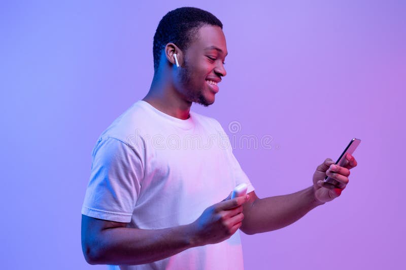 Gadżety techniczne. szczęśliwy czarny facet używający smartfona i słuchawek do słuchania muzyki