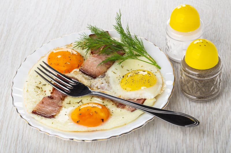Gaffeln på plattan med stekte ägg, bringan, dill, saltar shaker, pepparshaker på tabellen arkivbild Gaffeln på plattan med stekte ägg, bringan, dill, saltar shaker, pepparshaker på tabellen arkivbild