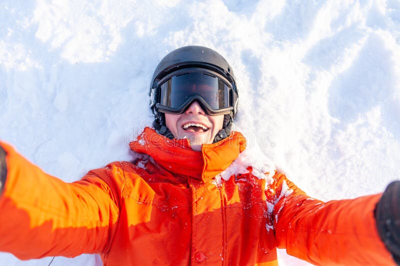 Gai mec en vêtements de ski se trouve sur la neige en hiver et prend selfie homme en casque de veste orange et lunettes au photos stock
