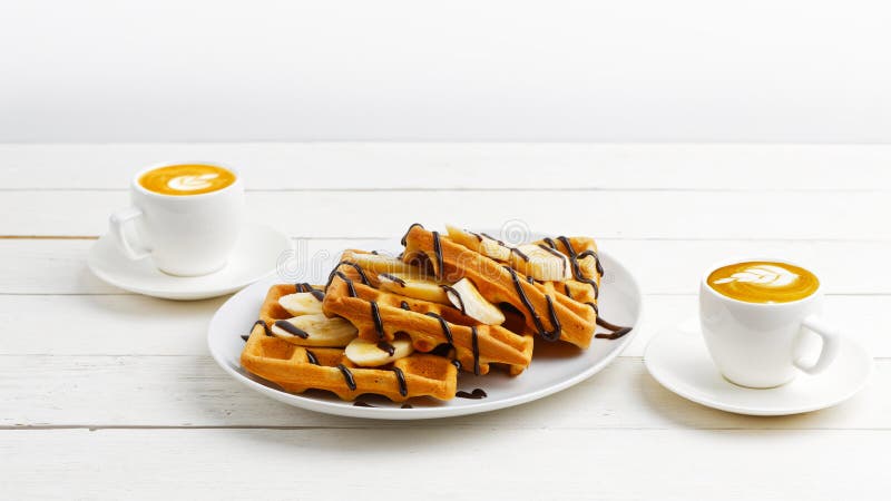Galletas belgas hechas en casa con las rebanadas del pl?tano rematadas con el chocolate y dos tazas de caf? en la tabla de madera imagenes de archivo Galletas belgas hechas en casa con las rebanadas del pl?tano rematadas con el chocolate y dos tazas de caf? en la tabla de madera imagenes de archivo