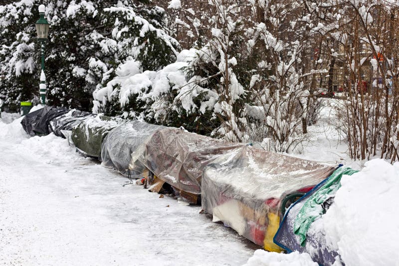 Roost of some homeless people on the bench of a public park. While we spend freezing nights in our cozy, warm homes many homeless people have to sleep outdoor only covered with some old plastic bags and tarps. Roost of some homeless people on the bench of a public park. While we spend freezing nights in our cozy, warm homes many homeless people have to sleep outdoor only covered with some old plastic bags and tarps.