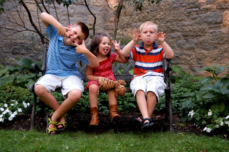 Three young children sitting on a bench making silly faces. Could be spring or summer. Three young children sitting on a bench making silly faces. Could be spring or summer.