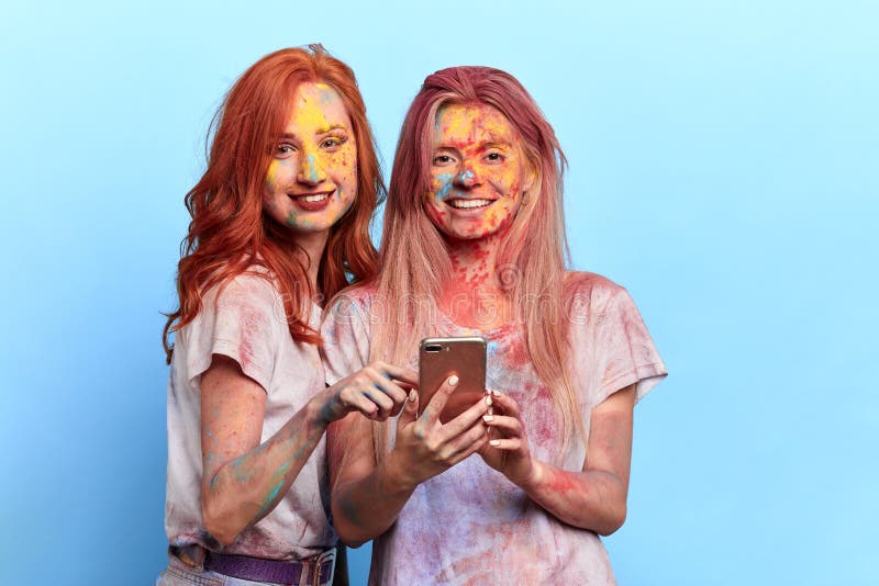 Galna roliga flickor med kulöra framsidor som rymmer smartphonen och poserar till kameran fotografering för bildbyråer Galna roliga flickor med kulöra framsidor som rymmer smartphonen och poserar till kameran fotografering för bildbyråer