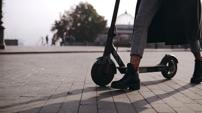 Gambe di una giovane camionista che cammina con il suo trasporto ecologico, motorino elettrico Camminando per le ragazze
