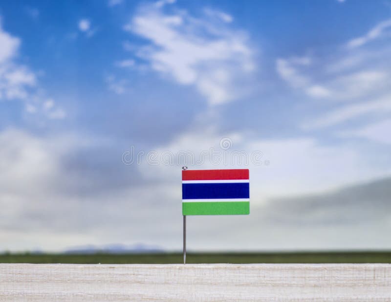 Gambia flag with vast meadow and blue sky behind it. royalty free stock image