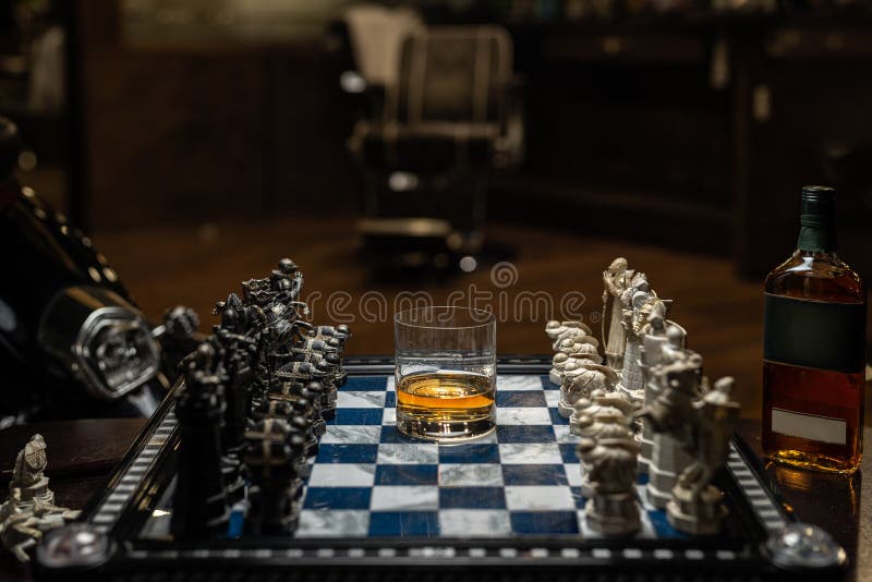 Focused man sipping alcoholic beverage while thinking about next chess move.  Stock Photo by DC_Studio