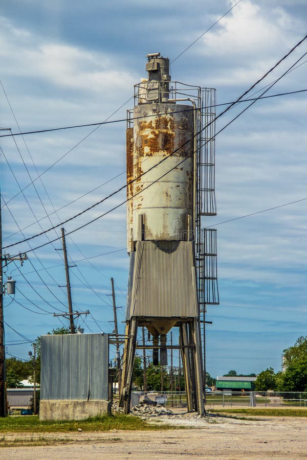 Old grungy rusty Silo for Concrete Batching Plant standing against blue cloudy sky with many electrical highlines near Cushing USA. Old grungy rusty Silo for Concrete Batching Plant standing against blue cloudy sky with many electrical highlines near Cushing USA.