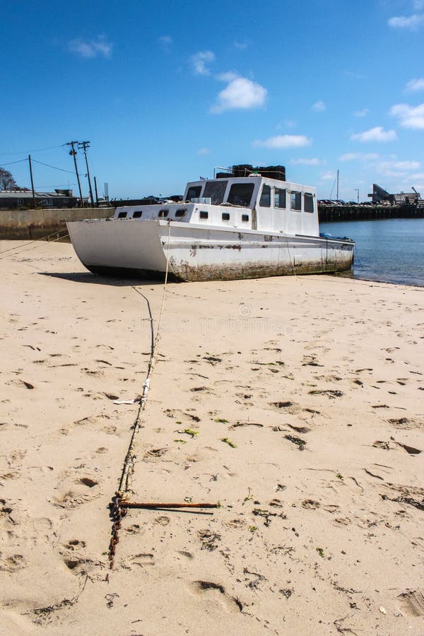 Gammal högdragen fiskebåt med hummerburar på övre delen bunden till stranden med stängning av kedja som binder den till arbetsdoc royaltyfri bild Gammal högdragen fiskebåt med hummerburar på övre delen bunden till stranden med stängning av kedja som binder den till arbetsdoc royaltyfri bild