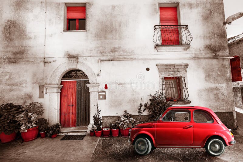 An old Italian house with a small subcompact old red car. Vintage scene. Potted plants and flowers at the entrance. Doors and windows red. Location: Castel Petroso. An old Italian house with a small subcompact old red car. Vintage scene. Potted plants and flowers at the entrance. Doors and windows red. Location: Castel Petroso