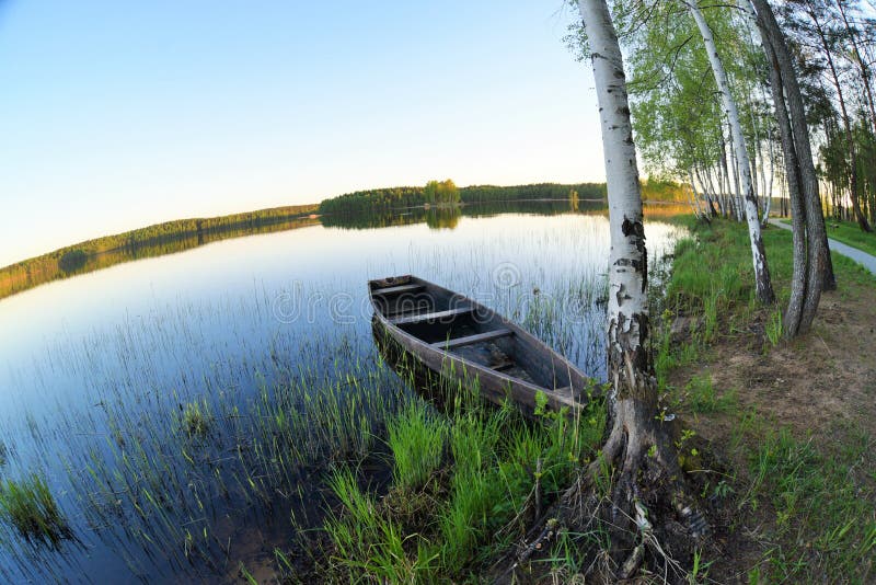Gammalt träfartyg på kusten av en skogsjö Idialistic landskap med vårnaturen och klar blå himmel arkivfoton Gammalt träfartyg på kusten av en skogsjö Idialistic landskap med vårnaturen och klar blå himmel arkivfoton