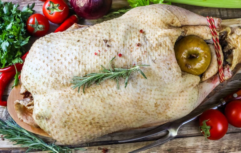 Raw goose, ready to cook, spices, apples, vegetables, greens on a wooden background. Top view. Holiday menu. Raw goose, ready to cook, spices, apples, vegetables, greens on a wooden background. Top view. Holiday menu.