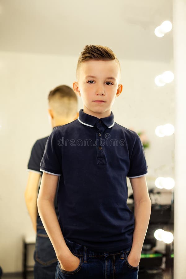 garçon de 10 ans dans un coiffeur après une coupe de cheveux à la mode  devant un miroir.Un petit enfant dans un salon de beauté regarde la caméra  poser Photo Stock 