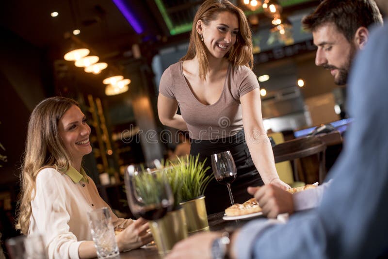 Garçonete bonita servindo grupo de amigas com comida no restaurante