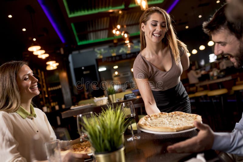 Garçonete bonita servindo grupo de amigas com comida no restaurante