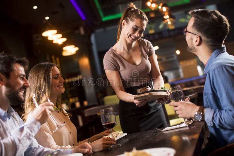 Garçonete bonita servindo grupo de amigas com comida no restaurante