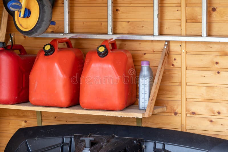 Garagehoek met drie rode plastic brandstofblikken, trap en sneeuwploeg voor atv met houten muur op achtergrond Benzinegas