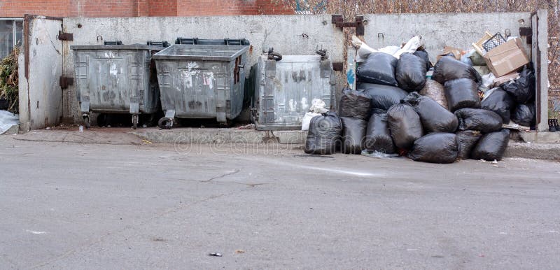 Garbage in black plastic bags in a heap and empty trash cans nearby. royalty free stock photos